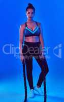 Challenge accepted. Full length shot of an attractive young sportswoman holding battle ropes against a blue background.