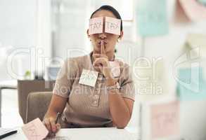 Tax evasion is a crime. Shot of a young businesswoman covered in sticky notes and holding her fingers on her lips while working on taxes in an office.