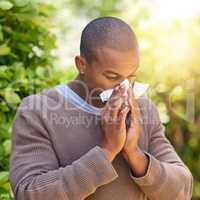 Sniffles, sneezes and wheezes. Shot of a young man blowing his nose outdoors.