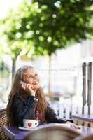 Ok, see you in a bit. A beautiful teen talking on her cellphone while sitting at a bistro.