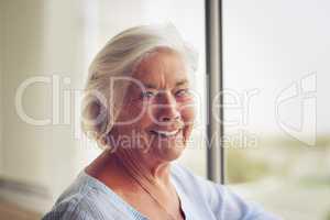 My age does not define my happiness. Portrait of a happy and relaxed senior woman standing next to a window indoors.