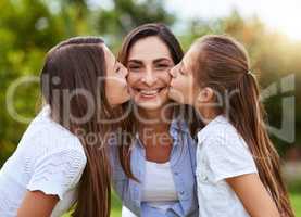 The girls of the family. Portrait of a cheerful young woman receiving a kiss on each cheek from her young daughters outside in a park during the day.