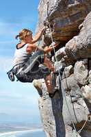 Adrenaline is pushing her to the summit. A young woman climbing up a rock face while framed against a blue sky.