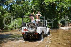 Taking their trip to some extreme terrain. Shot of a young couple driving through a river in their off-road vehicle.