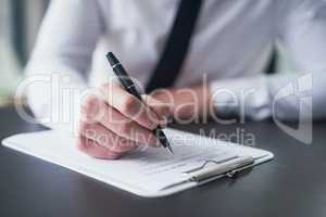 Ticking all the right boxes. Cropped shot of a businessman filling out paperwork on a clipboard while sitting at a table in an office.