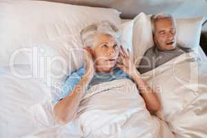 Youd have thought Id be used to his snoring. Cropped shot of a senior woman blocking her ears in frustration while her husband snores in bed beside her.