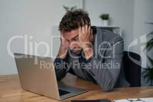 Stressed and frustrated with work. Portrait of an overwhelmed businessman sitting at his desk with his face in his hands.