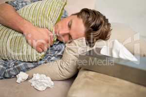 Im sick. I need someone to comfort me.... Shot of a sick young man lying on the sofa with tissues.