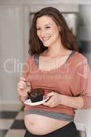 Pregnancy cravings. Cropped shot of a young pregnant woman eating a cupcake in the kitchen.