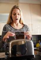 Looks like its going to be one of those days. Shot of a young woman removing a slice of burnt toast from a toaster at home.