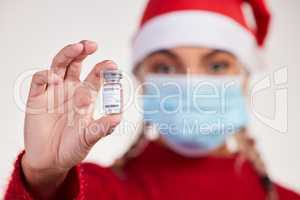 All I want for Christmas is a vaccine. Studio shot of a young woman holding vaccine and wearing a mask against a grey background.