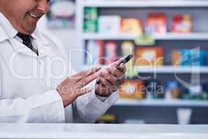 Always on the look out for new medical breakthroughs. Shot of an unrecognizable pharmacist using a cellphone in a pharmacy.