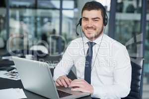 Happy to be or assistance. Portrait of a young customer service representative wearing a headset while sitting at his workstation in an office.