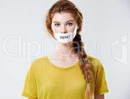 Use your voice. Cropped studio portrait of a young woman with a label saying speak covering her mouth.