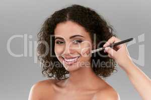 Make up is all about applying it correctly. Studio shot of a beautiful young woman applying foundation with a make up brush against a gray background.