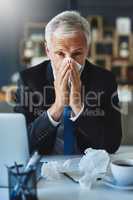 I have to take it easy today. Shot of a frustrated businessman using a tissue to sneeze in while being seated in the office.