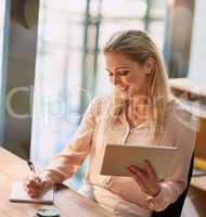 Juggling her analog and digital workflow. Shot of a smiling young businesswoman working on a digital tablet in an office.