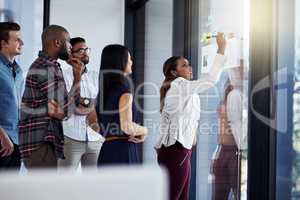 Her new plan of action has everyone intrigued. Shot of a young businesswoman giving a demonstration on a glass wall to her colleagues in a modern office.