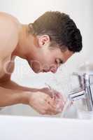 He knows how to keep it clean. Shot of a handsome young man washing his face at the bathroom sink.