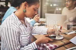 Always busy as usual. Shot of a focused young woman texting on her cellphone while being seated at a coffeeshop drinking a hot beverage.