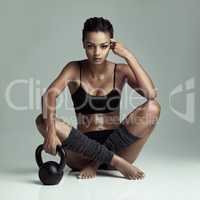 Taking a breather. Studio shot of a fit young woman sitting on the floor with a kettle bell against a gray background.