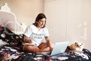 Im getting some great tips online. Shot of an attractive young woman making notes while using her laptop.