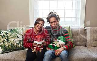 Even our dogs are in with the Christmas spirit. Portrait of a cheerful young couple holding their pet dogs while being seated on a sofa during christmas time at home.