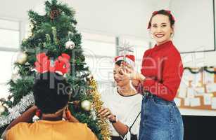 A Christmas tree isnt complete without the shining star. Portrait of an attractive young businesswoman decorating a Christmas tree with her colleagues at work.