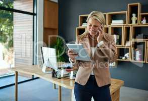 Merging tech with success. Shot of a mature businesswoman using a digital tablet while talking on a cellphone in an office.