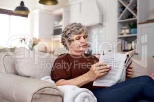 Chosen chapter of contentment. Shot of an elderly woman relaxing with a book on the sofa at home.