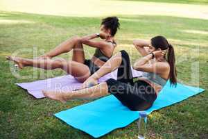 Beast mode activated. Full length shot of two attractive young women performing core exercises next to each other in the park.
