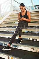 Got to sort my tunes first. Shot of a sporty young woman listening to music while exercising in the city.