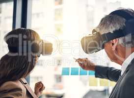Staying in control of their future success. Shot of two businesspeople wearing VR headsets while working with notes on a glass wall in an office.
