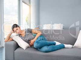 I think Im going to take easy today. Shot of a uncomfortable looking young woman holding a water bottle tightly while trying to get rest on a sofa at home.