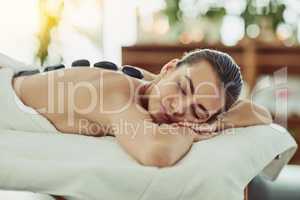 Taking it right to the muscles with heat. Shot of an attractive young woman getting a hot stone massage at a beauty spa.