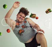 Dodge temptation - stick to your diet. Shot of an overweight man dodging food being thrown at him.