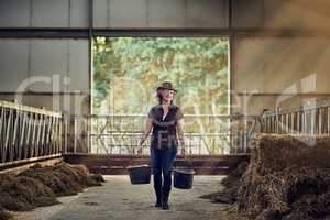Living the dream. Shot of a happy female farmer carrying buckets while walking out of a barn.