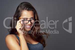 Heres lookin at you. Studio portrait of an attractive young woman peering over her glasses against a grey background.