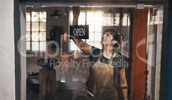 Supplying you with everything from A to steel. Shot of a young woman hanging an open sign at the entrance of a foundry.