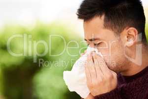 Flu season is here. Cropped shot of a young man blowing his nose outside.