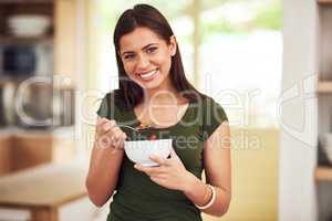 Health is happiness. Portrait of a happy young woman eating a bowl of muesli while standing in her kitchen.