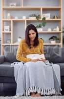 This pain is unbearable. Full length shot of an attractive young woman suffering from stomach cramps while sitting on a sofa at home.