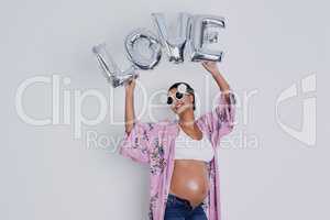So much love for someone I havent even met yet. Studio shot of a beautiful young pregnant woman holding up a word balloon that reads love against a gray background.