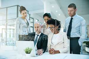 Trying to convince his team to agree with him.... Shot of a group of businesspeople coming together to work on something on a laptop.