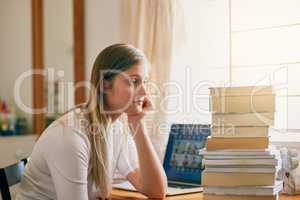 Thats an overwhelming amount of information. Shot of a young woman looking overwhelmed by the pile of books on her desk.