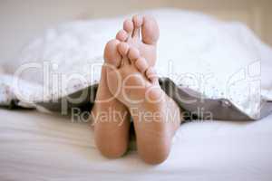 Sleeping is mandatory on weekends. Shot of an unrecognizable mans feet poking out of the bed sheets.