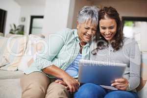 Bringing mom up to speed. Shot of a young woman showing something to her mother on her tablet while they sit on a sofa together.