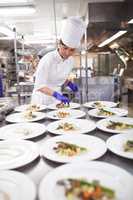 Capable hands in the kitchen. Shot of a chef plating food for a meal service in a professional kitchen.