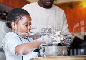 Daddys little baker. Shot of a father teaching his daughter how to bake in the kitchen at home.