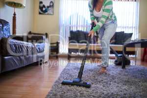 Her home is always neat and tidy. Shot of a young woman vacuuming a carpet at home.